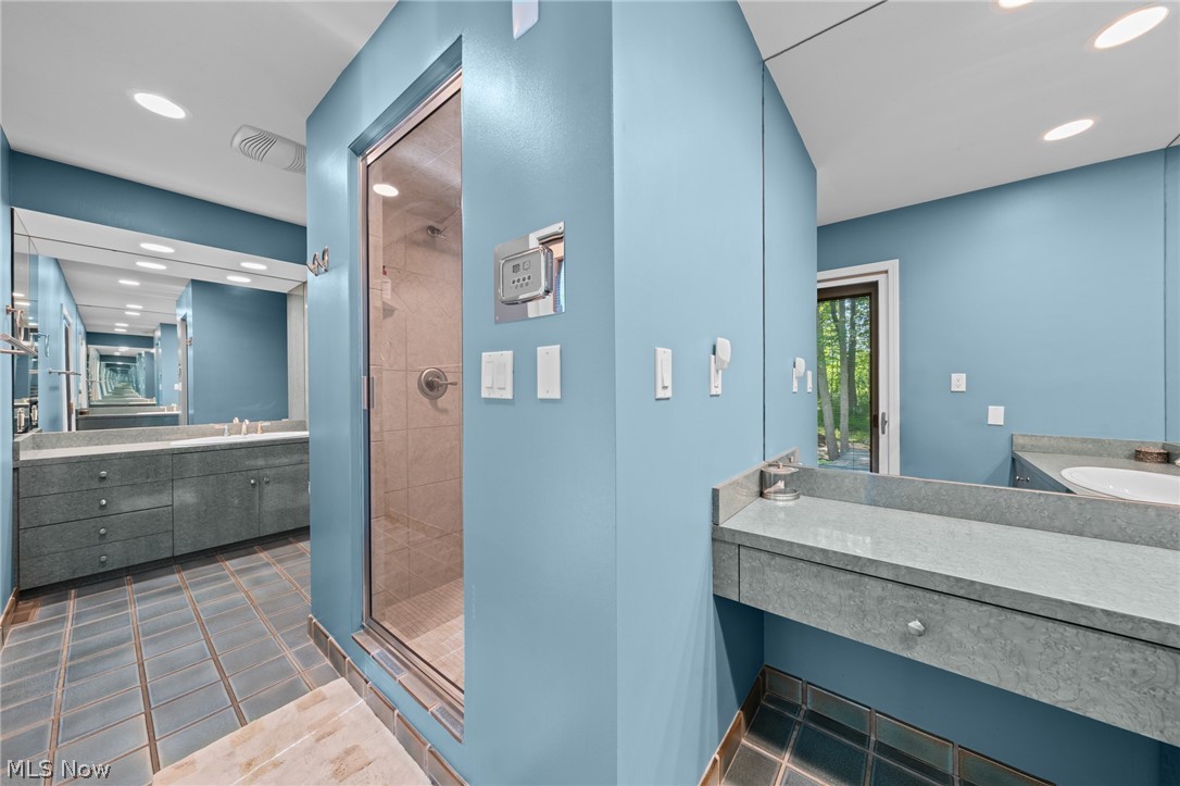 Bathroom with a glass shower, gray stone vanities, blue walls, and a glass door to the wooded outdoors.