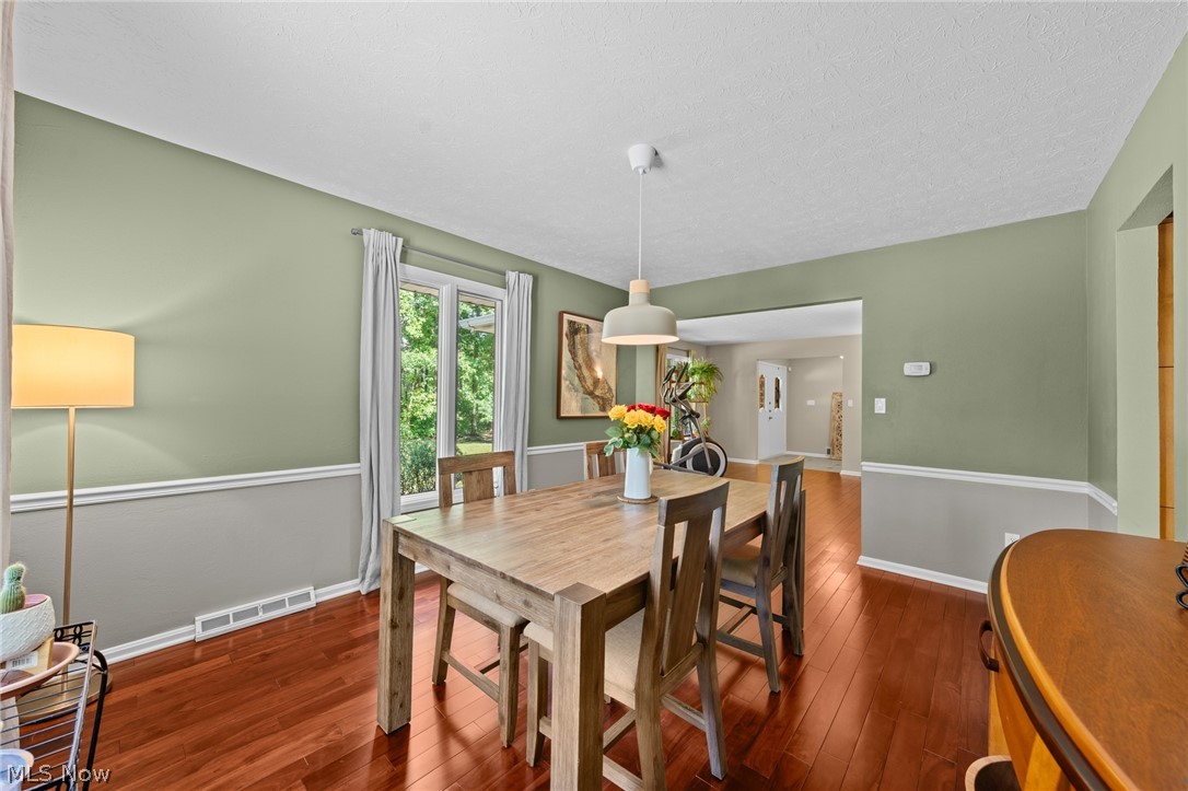 Dining room with a wooden table, reddish hardwood floors, and sage green walls.