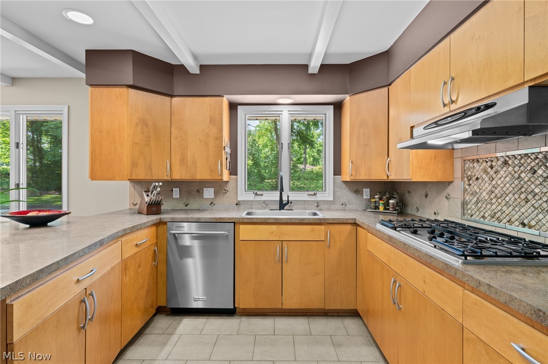 Kitchen with honey-colored cabinets, a gas cooktop, and a sink beneath a window overlooking trees.