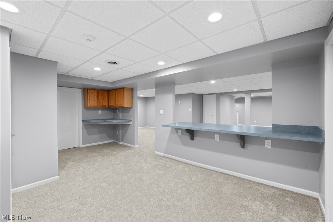 Finished basement recreation area with a long counter, wooden cabinets, and carpet.