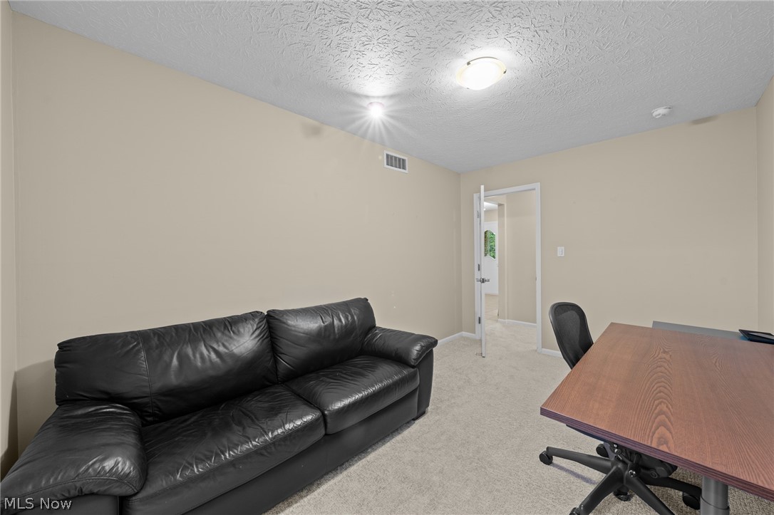 Office with a black leather sofa and wood desk beside an open doorway.