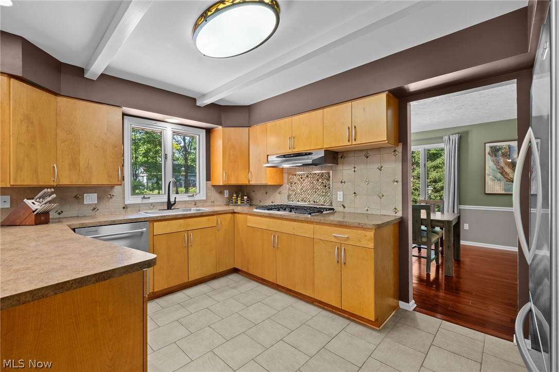 Kitchen with honey-colored cabinets, tiled backsplash, gas cooktop, and a window overlooking trees.