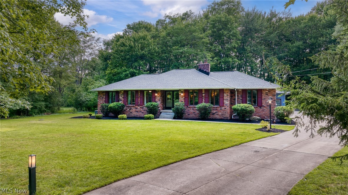 Brick ranch home with a broad lawn, concrete driveway, and mature trees.