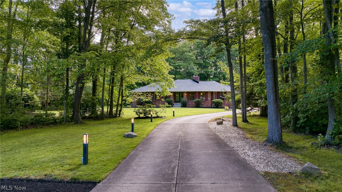 Brick ranch home nestled among mature trees at the end of a curved driveway.