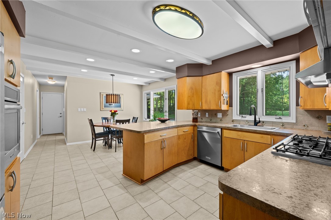 Kitchen with a large island, honey-colored cabinets, stainless steel appliances, and windows overlooking greenery.