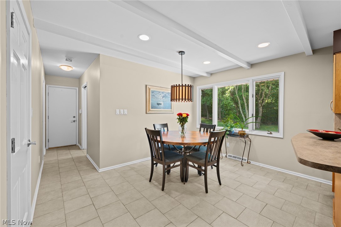 Dining area with a round wooden table, dark chairs, and large windows overlooking trees.