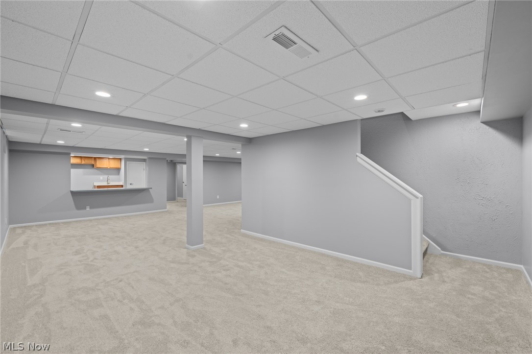 Finished basement with carpet, a kitchenette, a support column, and stairs.
