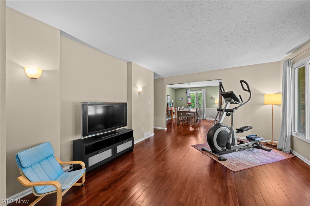 Living room with hardwood floors, an elliptical trainer, and an open view into the dining area.