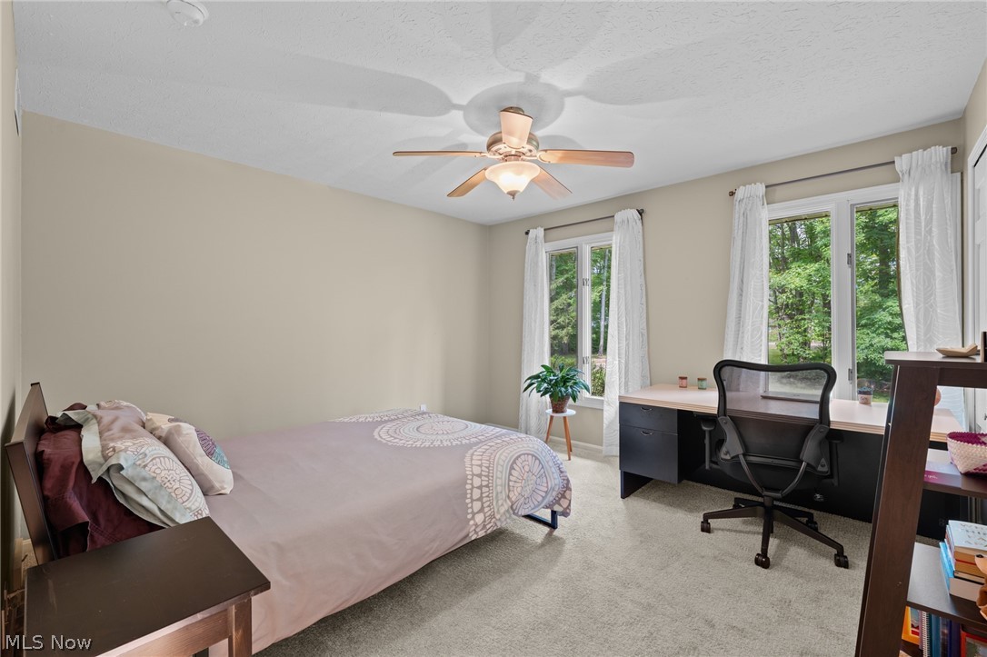 Furnished bedroom with a desk beside large windows overlooking leafy trees.