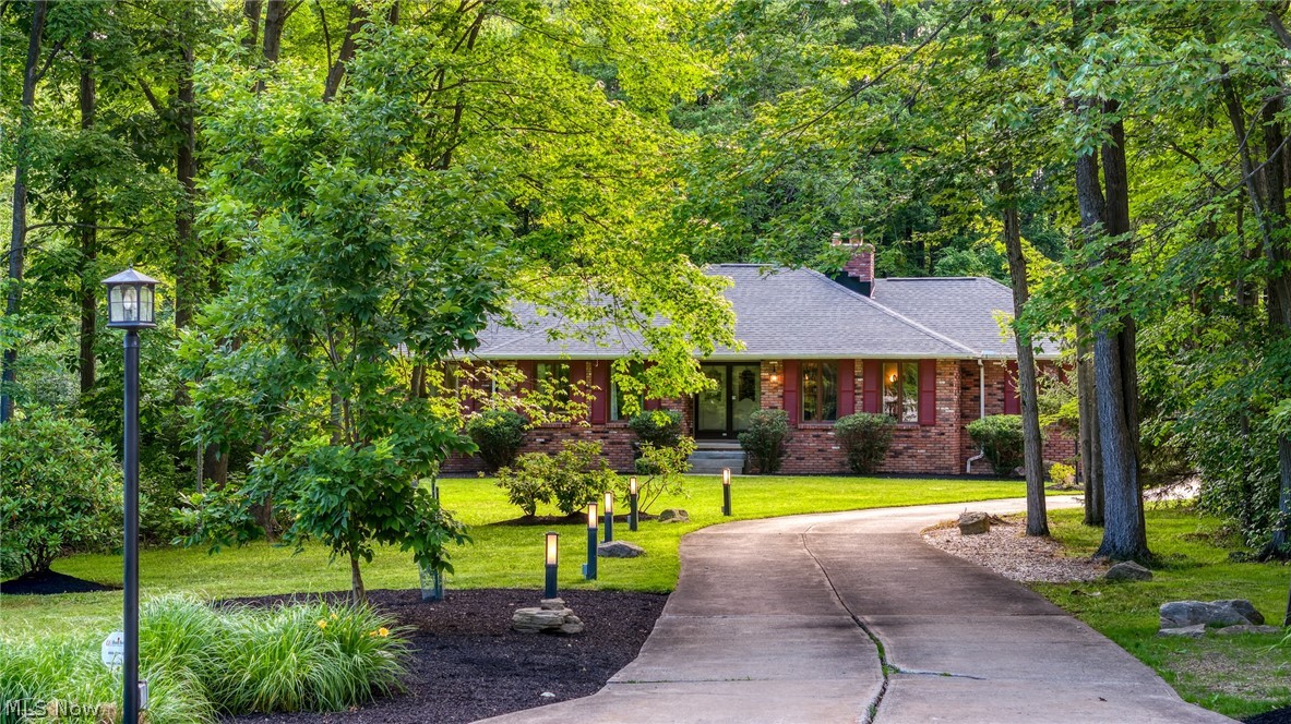Brick ranch home framed by mature trees, with a curved driveway and landscaped lawn.
