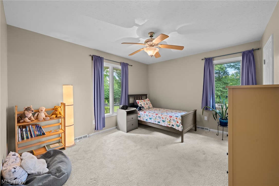 Bedroom with a single bed, purple curtains, a ceiling fan, and a bookshelf with stuffed animals.