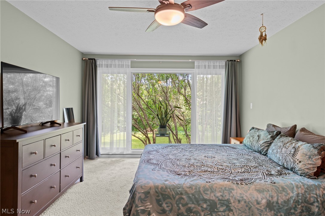 Furnished bedroom with patterned bedspread, ceiling fan, and sliding glass doors overlooking trees.