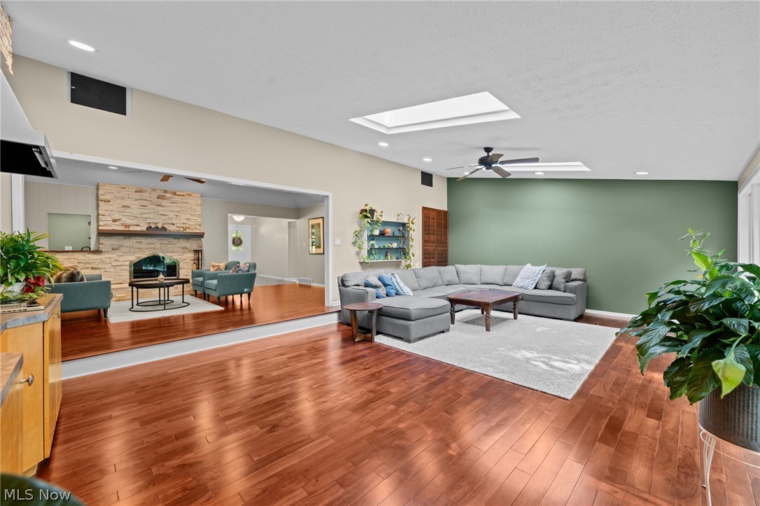 Living room with reddish hardwood floors, gray sectional, green accent wall, and adjoining stone-fireplace sitting area.