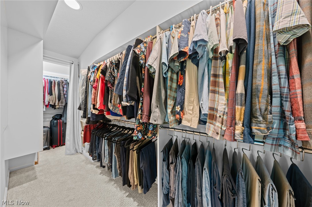 Walk-in closet with extensive hanging clothes and luggage at the far end.