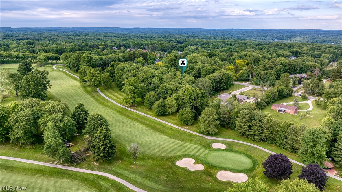 Aerial view of a manicured golf course, wooded landscape, and nearby homes.