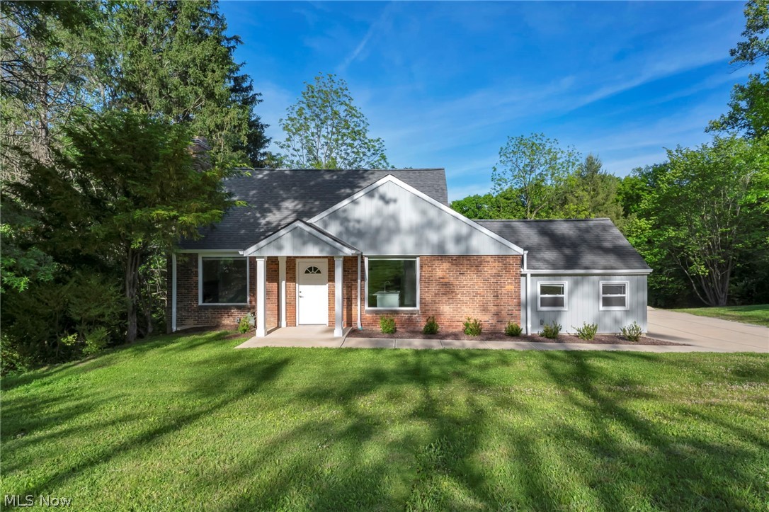 Single-story brick home with gray siding, a covered entry, mature trees, and a broad green lawn.