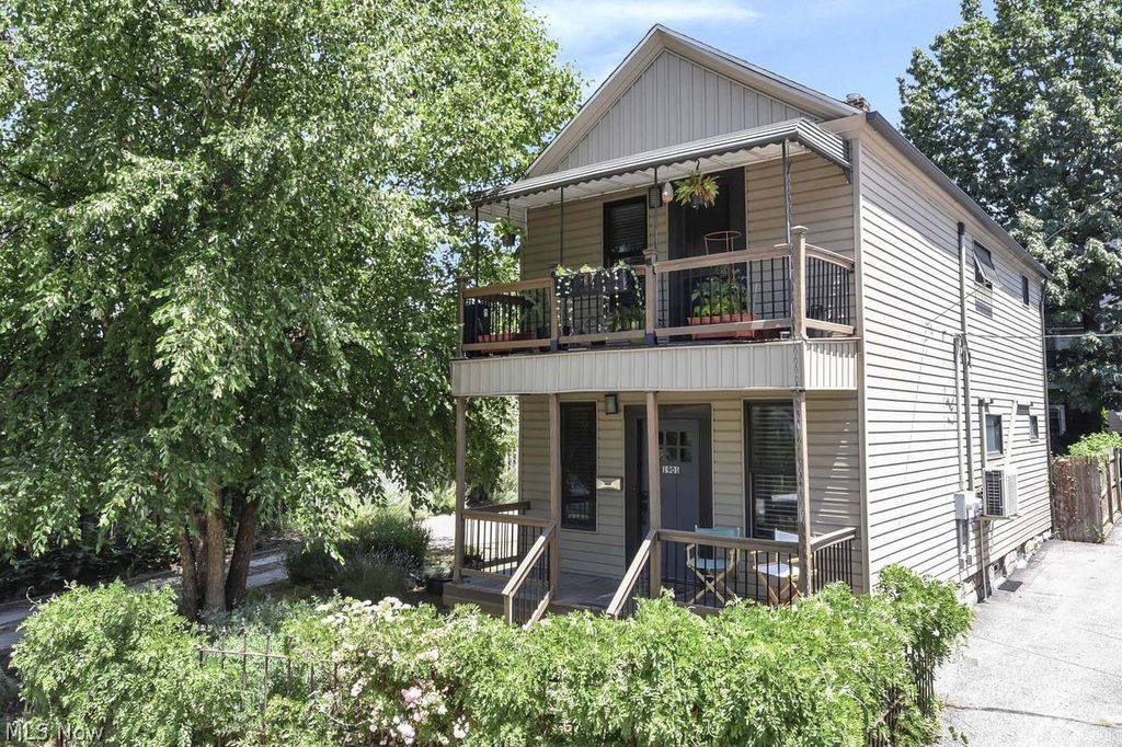 Two-story house with upper and lower balconies, mature trees, and a side driveway.