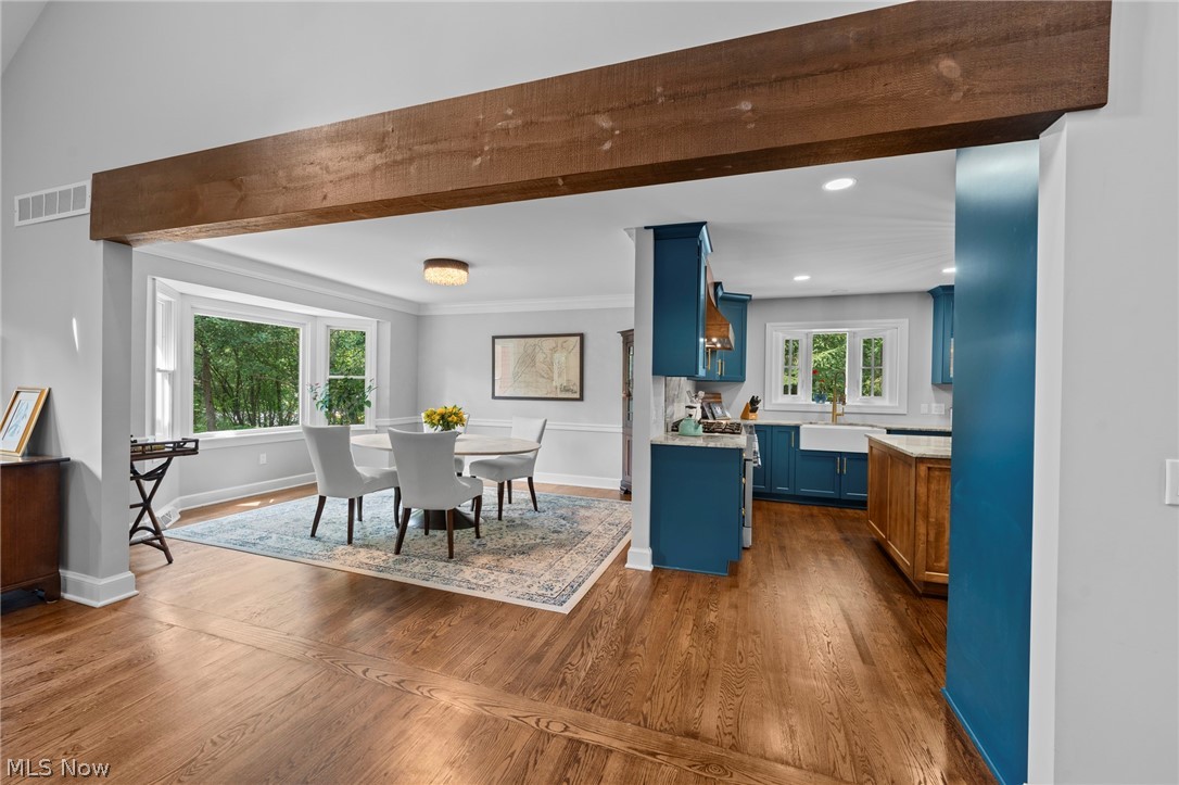 Dining room and kitchen with blue cabinetry, hardwood floors, and a large exposed wood beam.