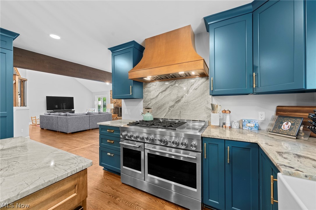Kitchen with blue cabinets, marble surfaces, a stainless-steel range, and a wood range hood.