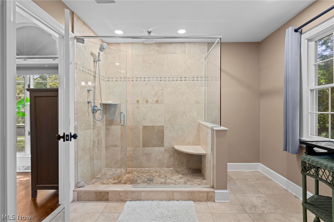 Bathroom with a large glass-enclosed tiled shower, built-in bench, and window.
