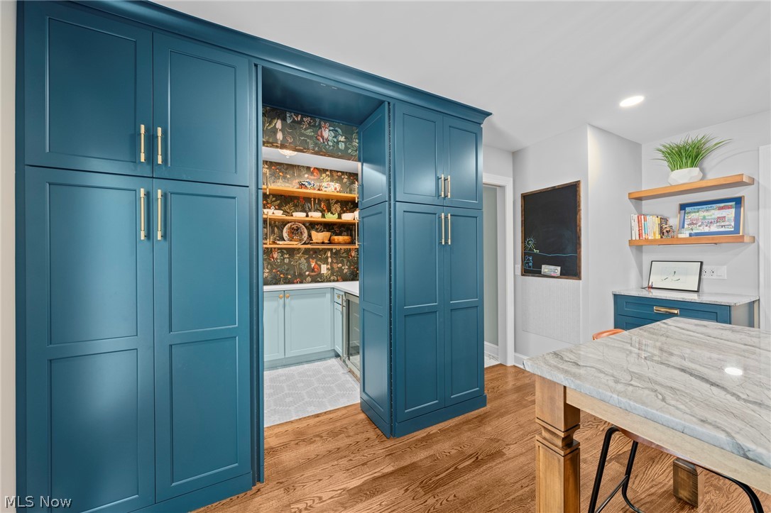 Kitchen with teal pantry cabinetry, patterned wallpaper, display shelves, and a marble-topped table.