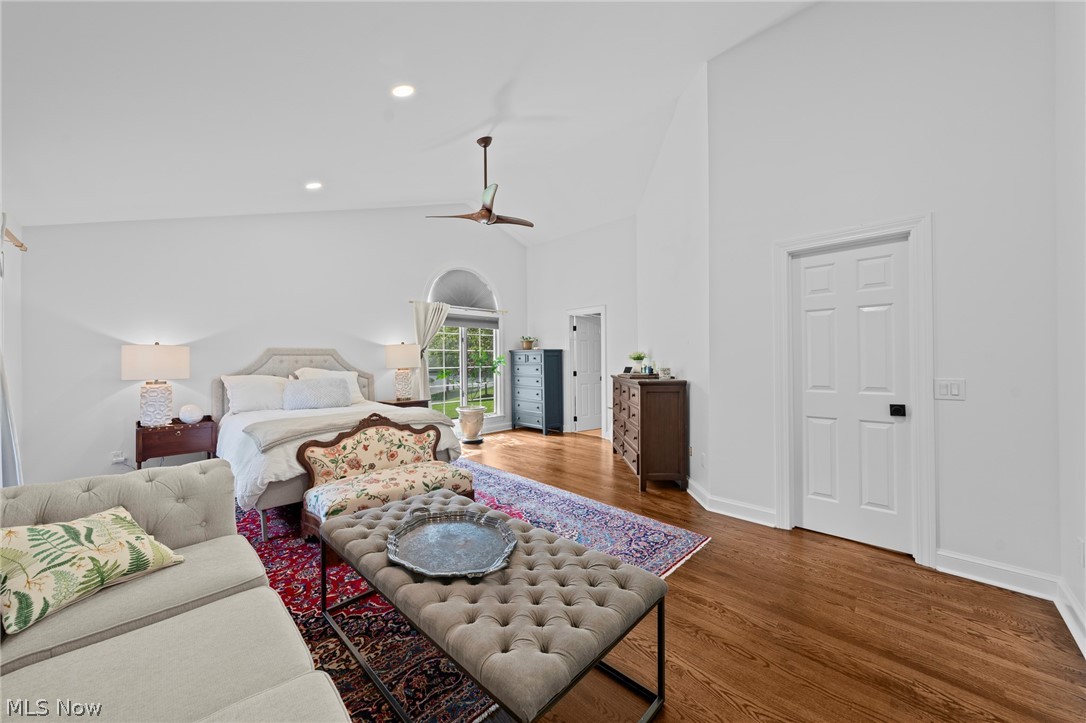 Bedroom with a sitting area, vaulted ceiling, arched window, and hardwood floors.