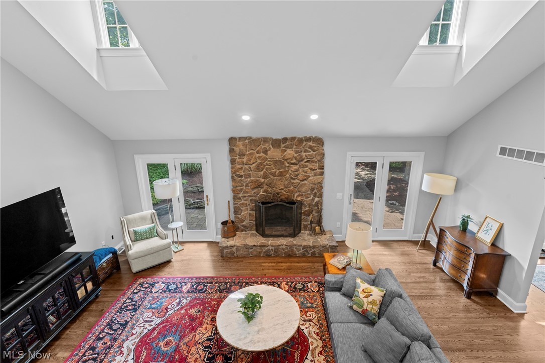Living room with a stone fireplace, skylights, patio doors, and a colorful patterned rug.