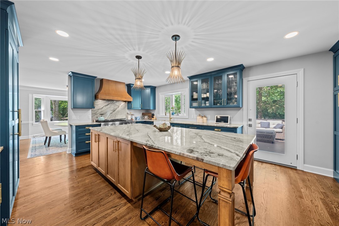 Kitchen with blue cabinetry, a large marble-topped island, leather stools and a sculptural wood range hood.