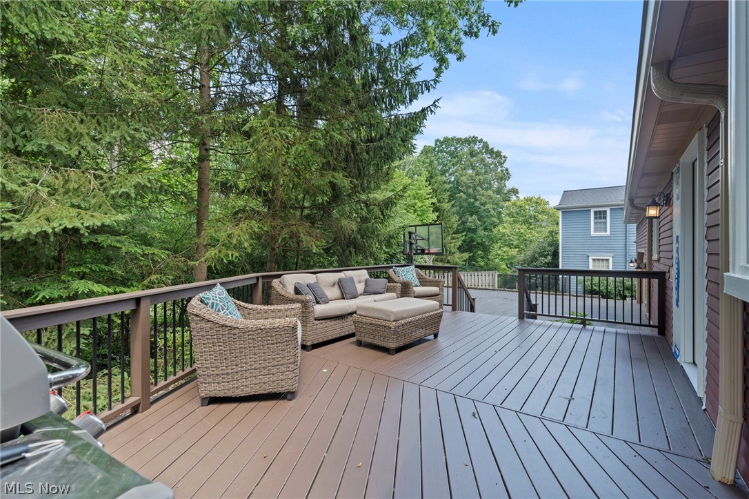 Raised deck with wicker seating, a barbecue grill, and a basketball hoop among mature trees.