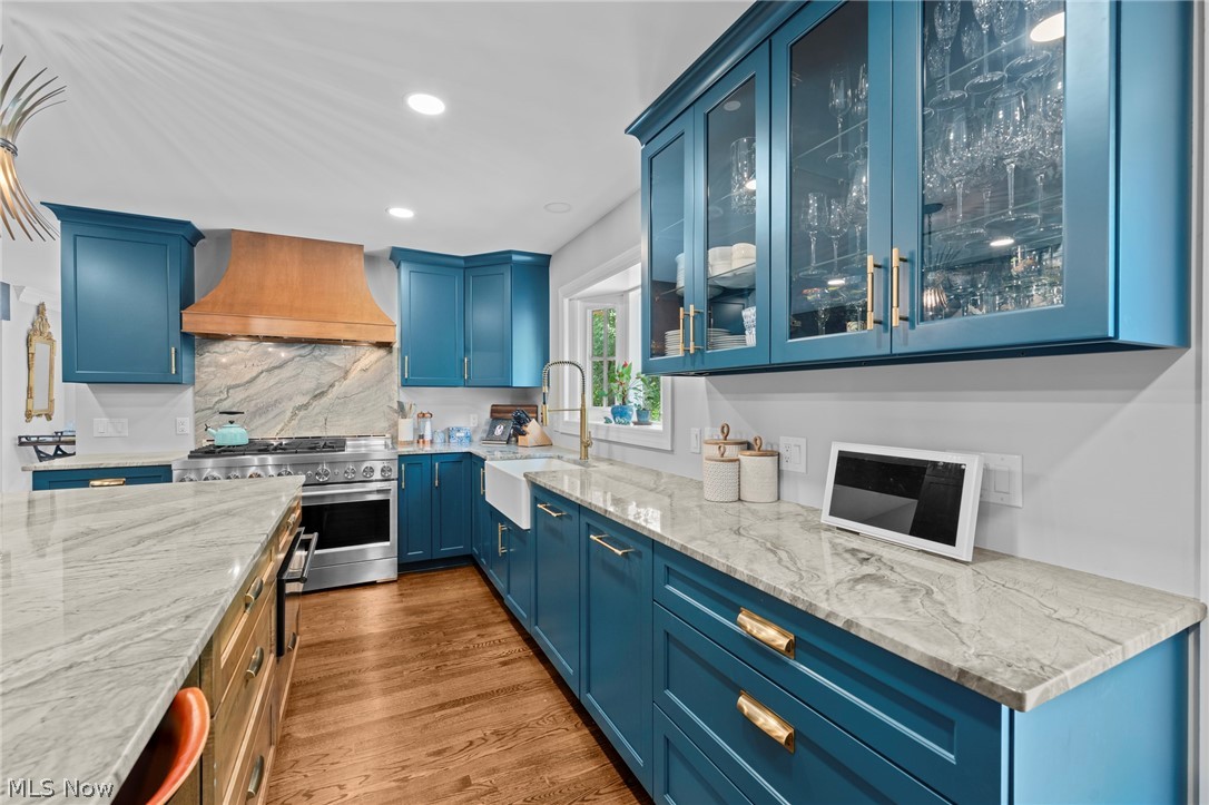 Kitchen with deep blue cabinetry, glass-front cupboards, marble counters, and a copper-toned range hood.