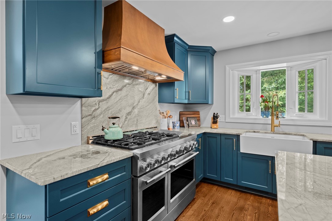 Kitchen with blue cabinets, veined stone counters, a stainless-steel range, and a farmhouse sink beneath a window.