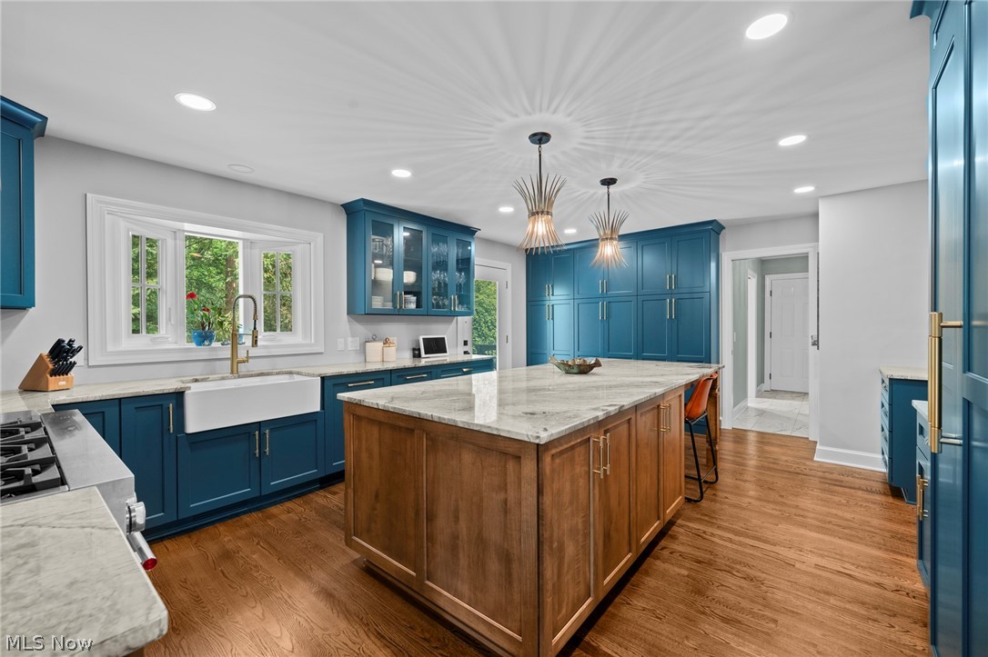 Kitchen with teal cabinetry, farmhouse sink, and a large wood-paneled island with a stone countertop.
