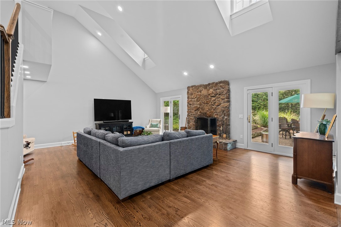 Furnished living room with vaulted ceiling, stone fireplace, and doors opening to a patio.