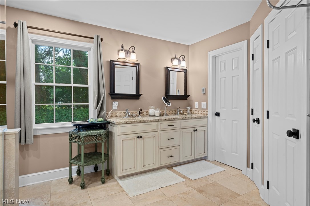 Bathroom with a cream double vanity, granite counter, and large window overlooking trees.