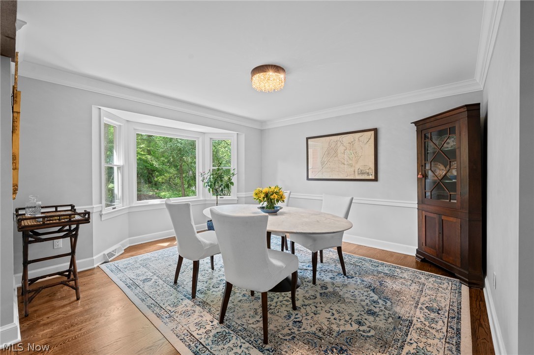 Dining room with a round table, bay windows overlooking trees, and a dark wood china cabinet.