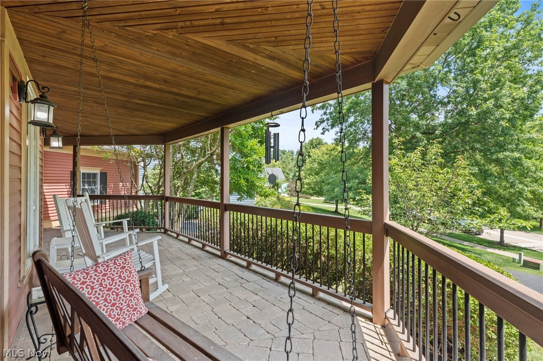Covered porch with white rocking chairs, stone pavers, and a leafy yard view.