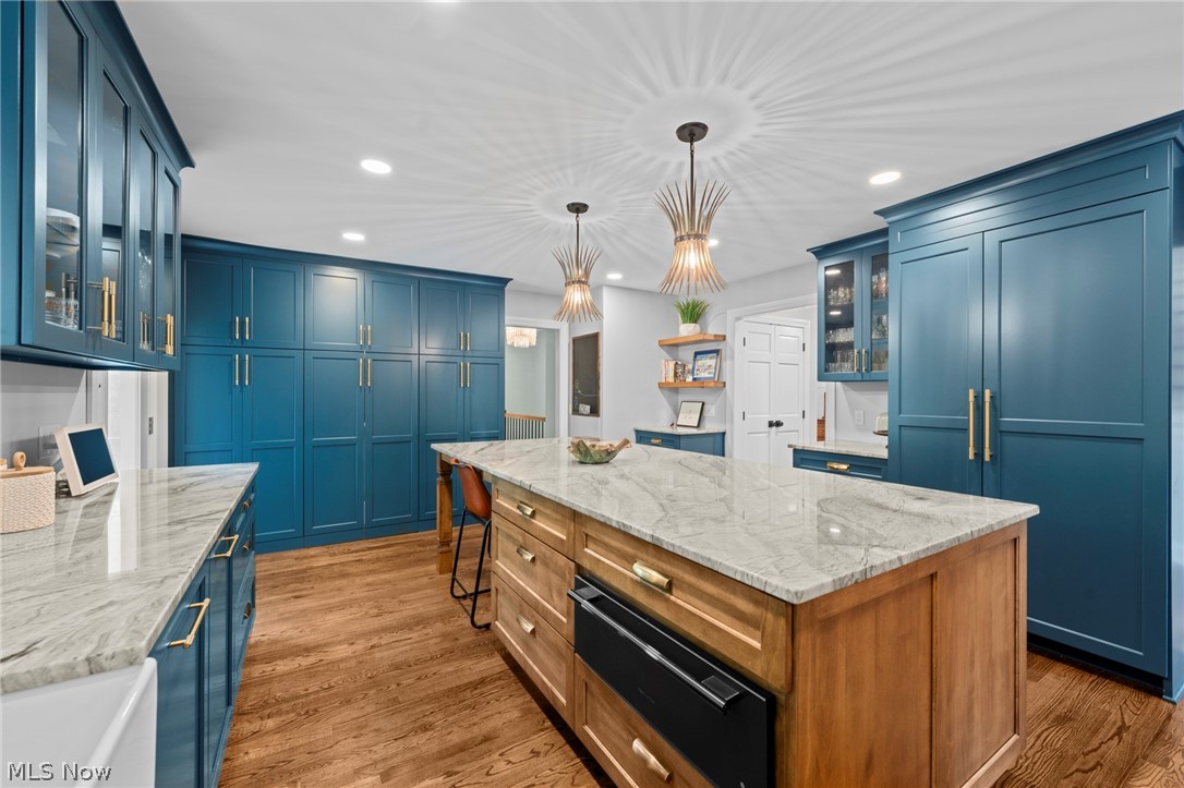 Kitchen with deep blue cabinets, a large marble-topped wood island, and sculptural pendant lights.