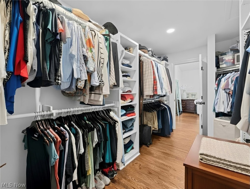 Walk-in closet with extensive clothing racks, white shelving, wood flooring, and a dresser.