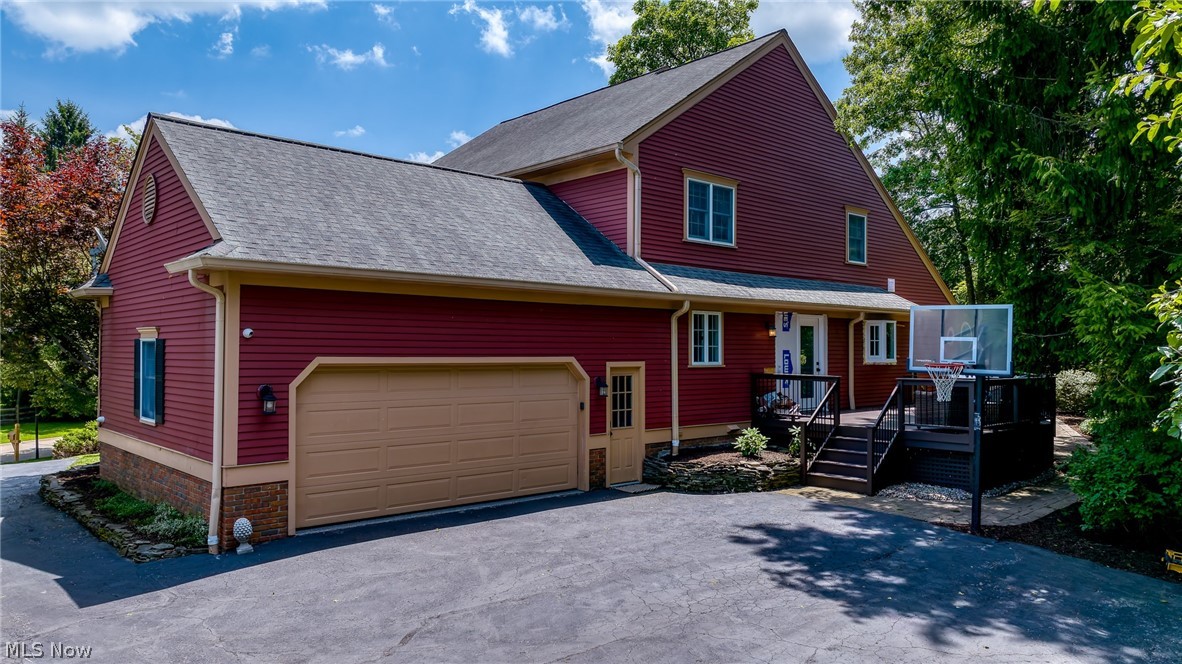 Red-sided home with attached garage, raised deck, and basketball hoop by the driveway.