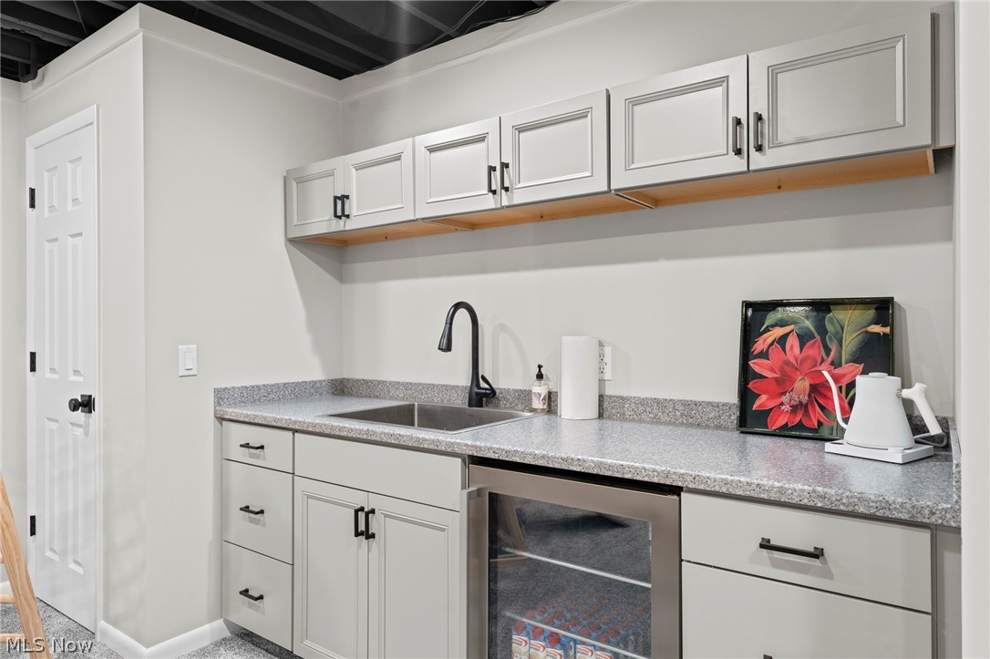 Wet bar with white cabinetry, a speckled countertop, sink, and glass-front beverage refrigerator.