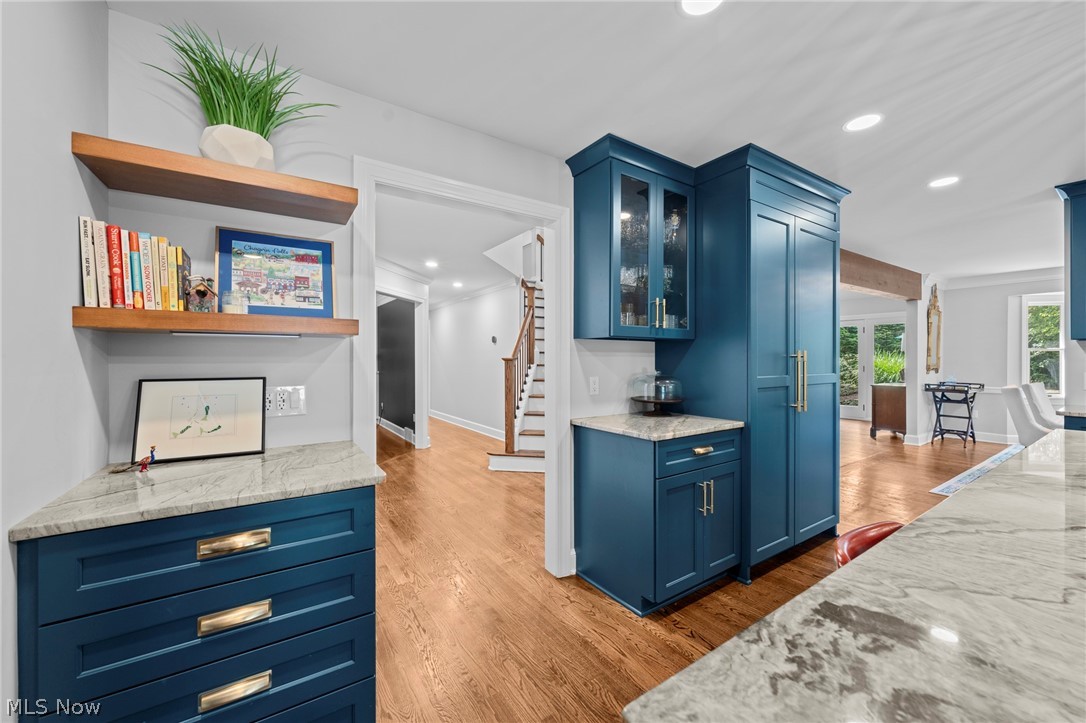 Kitchen with deep blue cabinets, marble counters, and open wood shelves beside a hardwood-floored dining area.