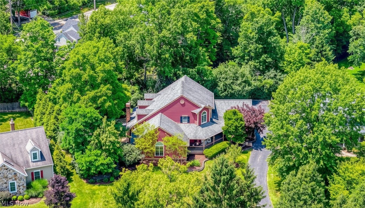 Aerial view of a red home surrounded by mature trees, gardens, and a curved driveway.