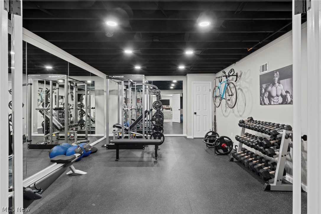 Home gym with mirrored walls, strength-training equipment, a dumbbell rack, and a bicycle mounted on the wall.