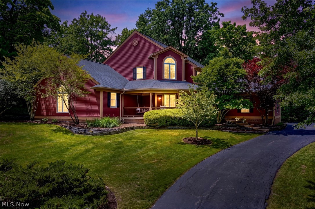 Red-sided home with a covered porch, mature trees, and a curved driveway at dusk.