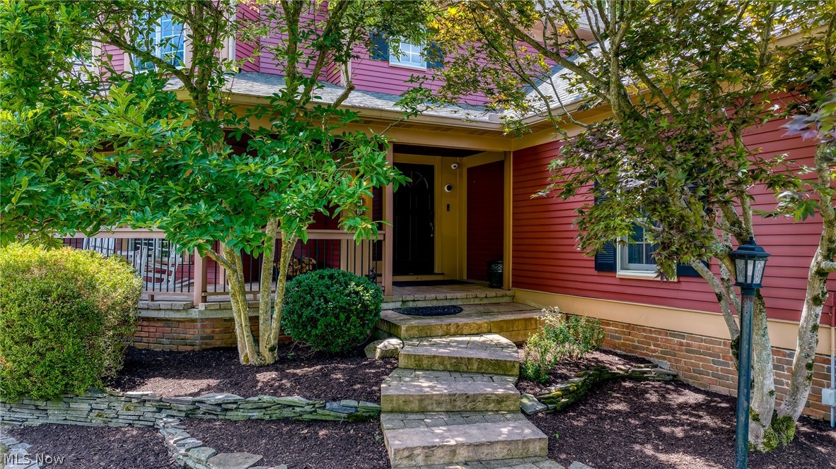 Home entrance with red siding, a covered porch, and stone steps through landscaped gardens.