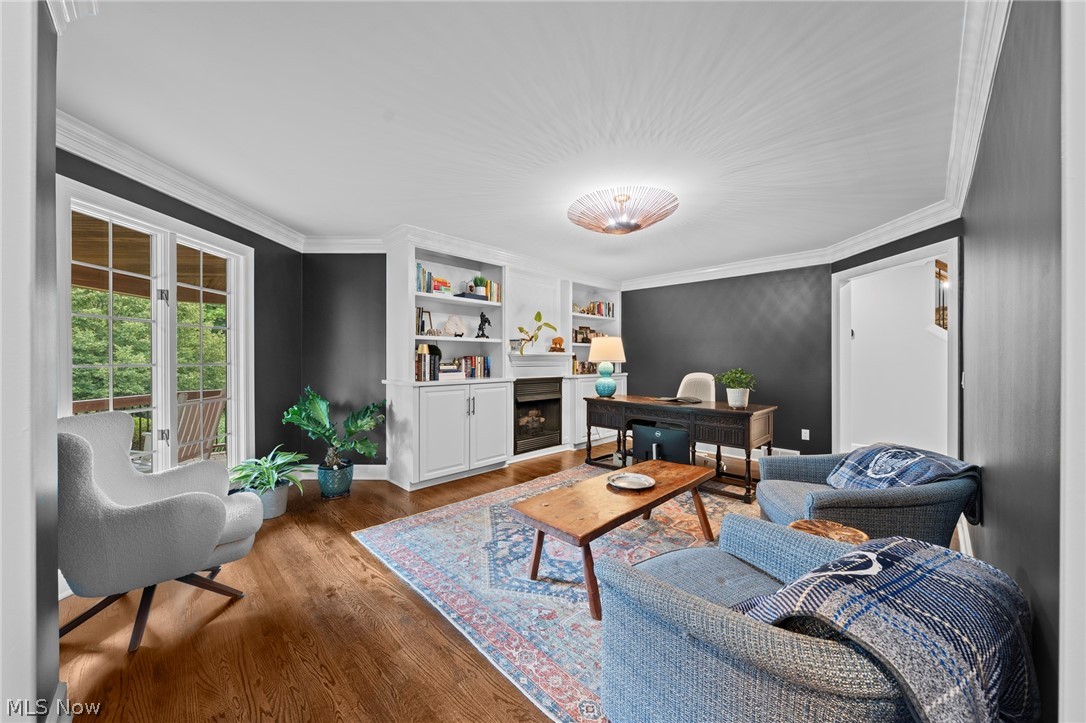 Home office with built-in bookshelves, fireplace, dark desk, blue seating, and hardwood floors.