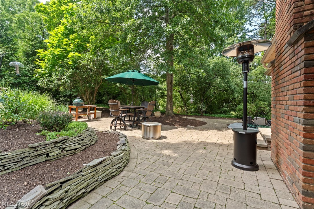 Stone-paved patio with umbrella-covered dining set, patio heater, and mature trees.