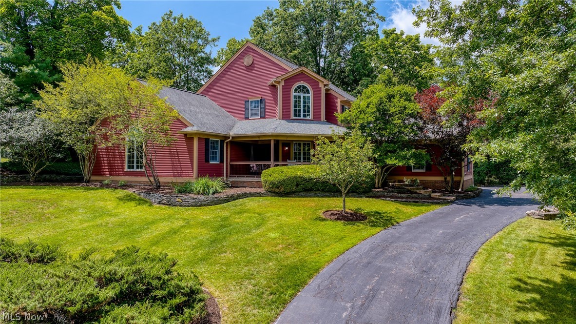 Red two-story home with covered porch, landscaped lawn, mature trees, and curved driveway.