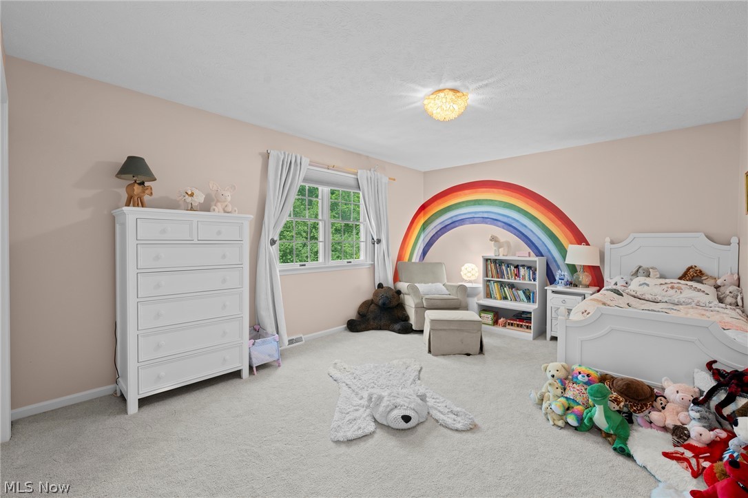 Child’s bedroom with a rainbow mural, white bed, stuffed animals, and a window overlooking greenery.