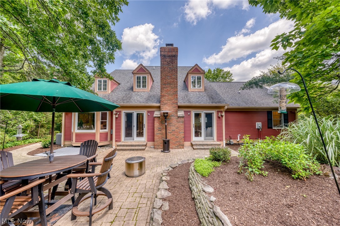 Home’s rear patio with outdoor dining furniture, green umbrella, and landscaped garden beds.